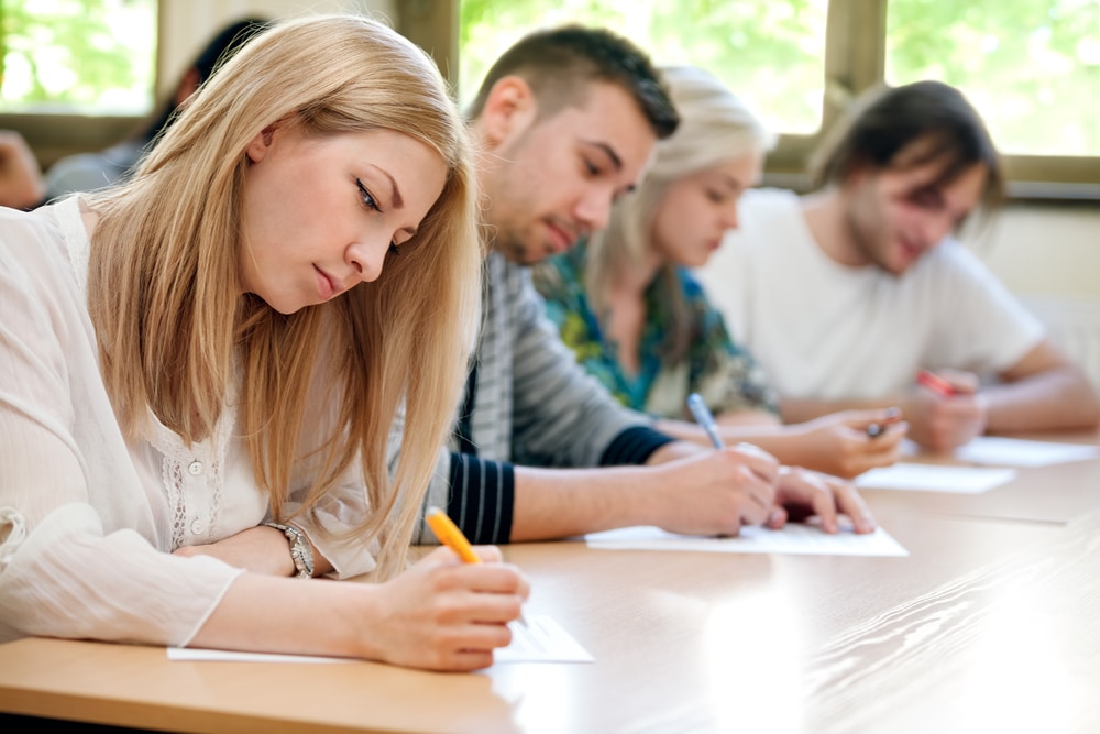 Four students taking an exam at a long, shared table