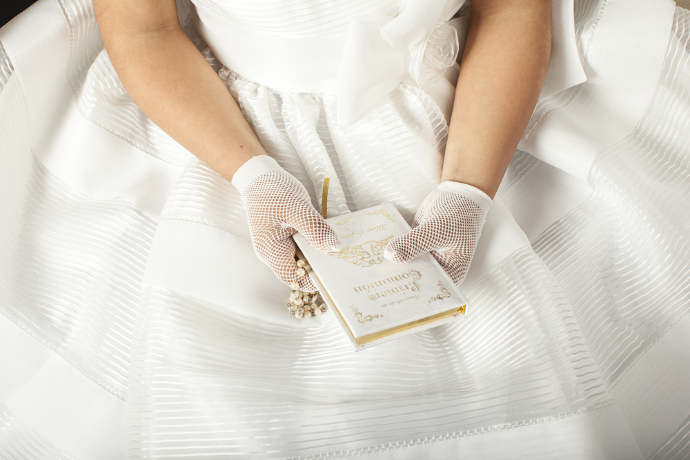 Close-up of young girl wearing a white dress and holding a prayer book for her first communion
