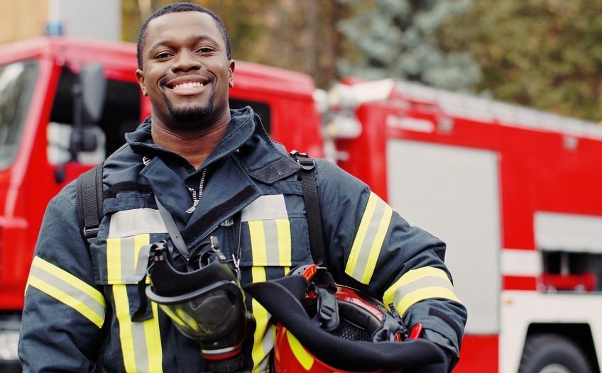 Firefighter in uniform smiling in front of a fire truck