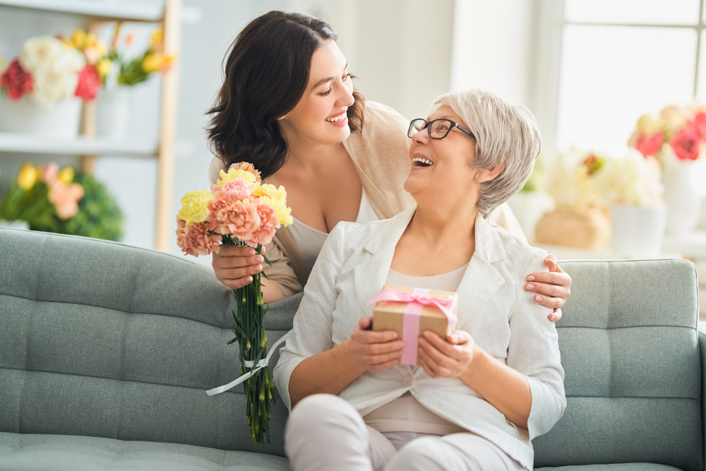 Woman giving her godmother flowers and a gift for Mother's Day