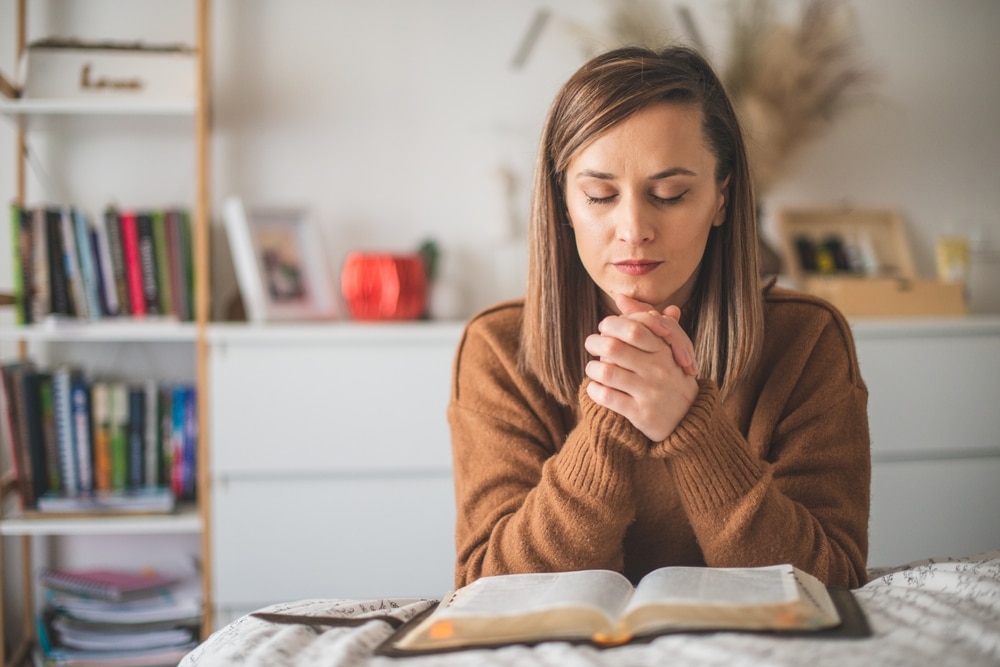 Woman kneeling at her bedside to pray