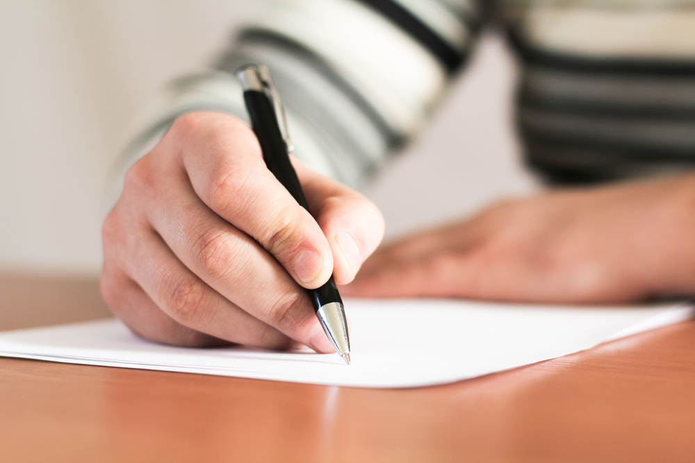 Close-up of a person's hand writing a letter with pen and paper